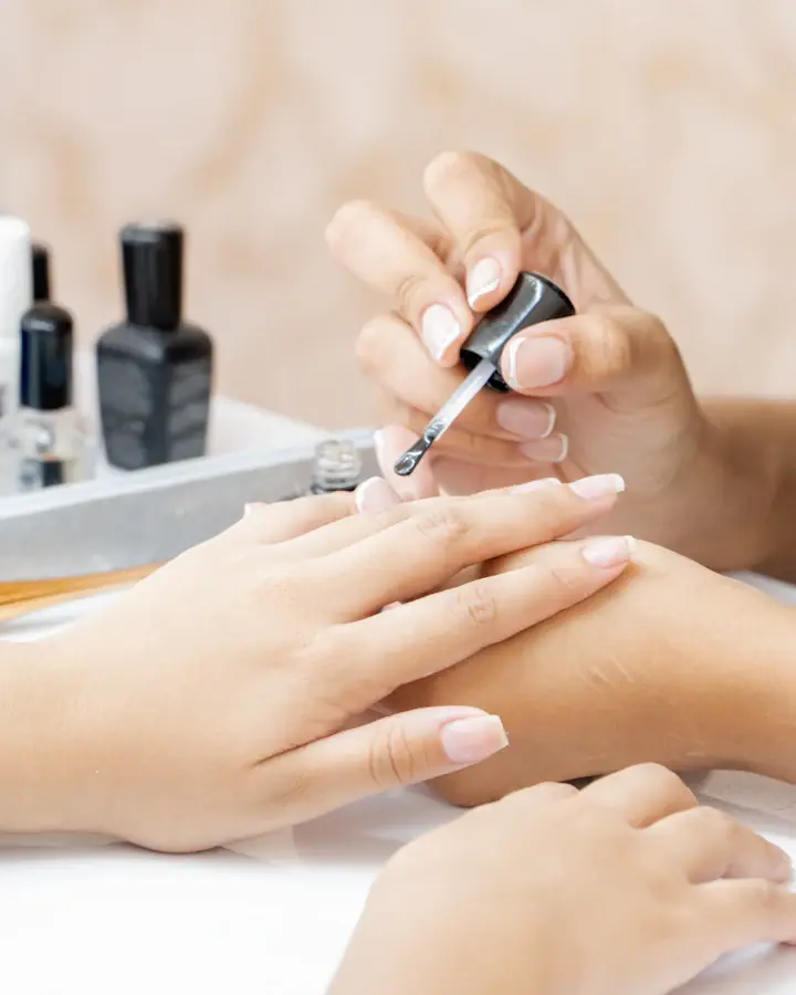 Manicure cuidando das unhas de uma cliente, com os esmaltes na bancada